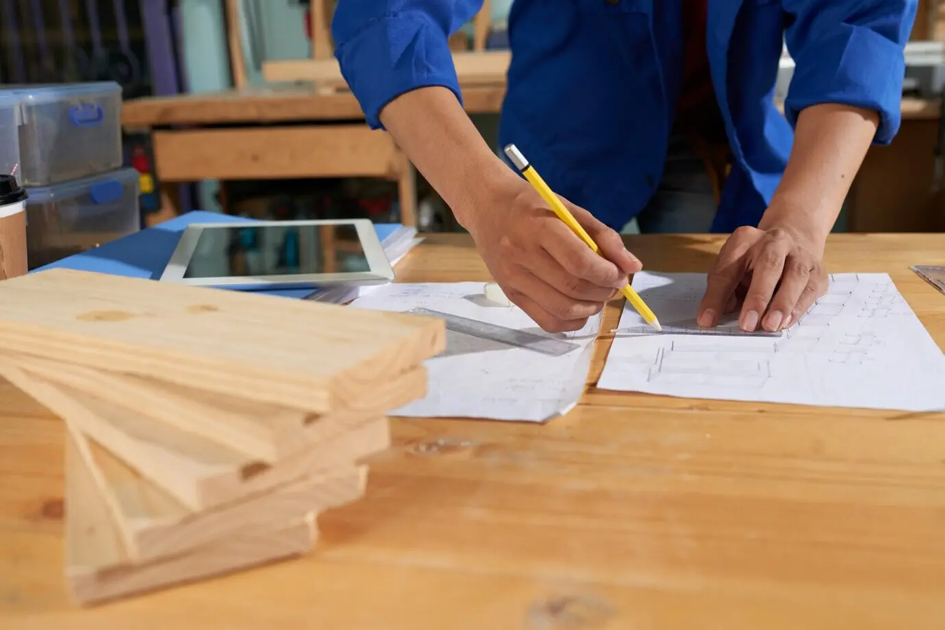 Cropped view of a man wearing a blue overall, drawing furniture on the sheet of paper.